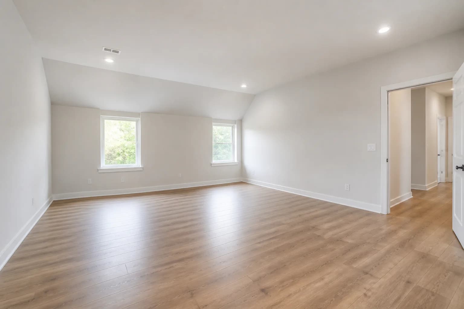 Completed empty new-construction bonus room with a sloped ceiling, two windows, and an open doorway