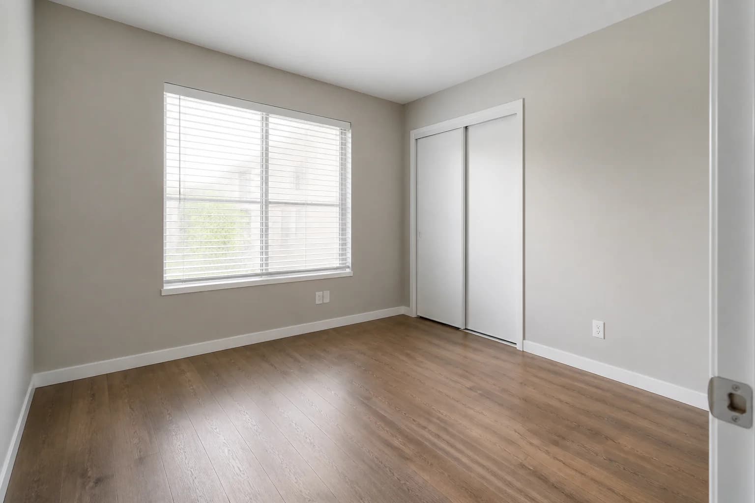 Empty rental bedroom with window blinds, sliding closet doors, and wood floor