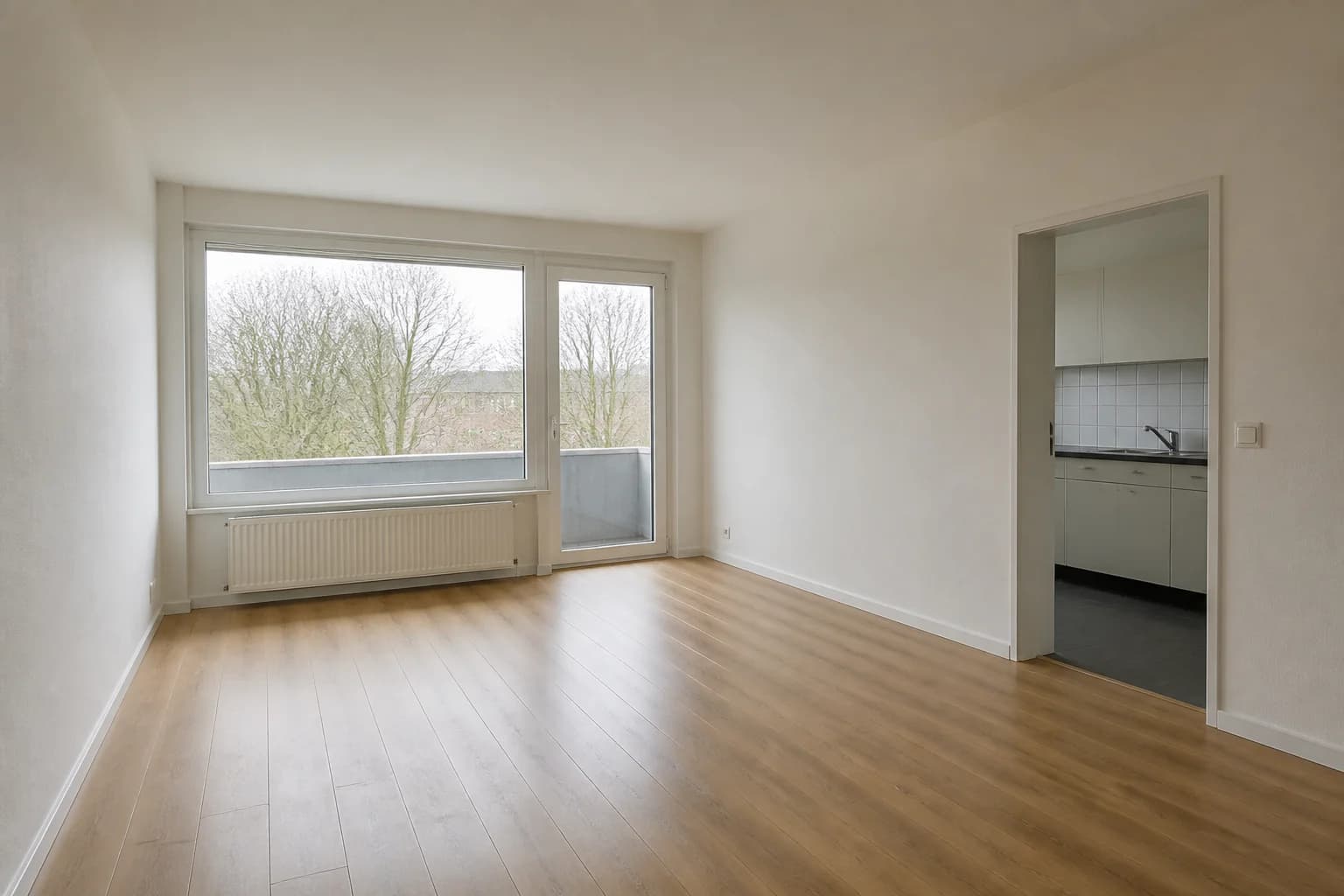 Vacant rental apartment living room with oak floor, balcony door, and kitchen doorway