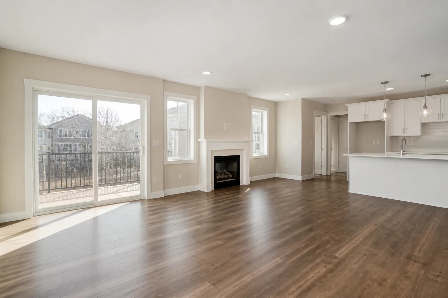Vacant townhouse open-plan family room with patio doors, fireplace, dark wood floor, and white kitchen
