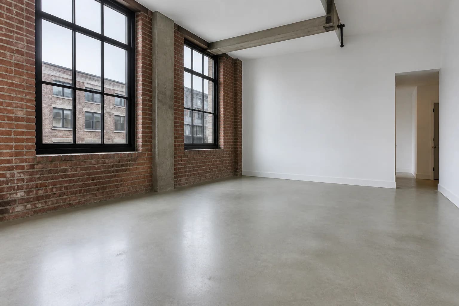 Empty urban loft living room with exposed brick, concrete flooring, and tall black-framed windows